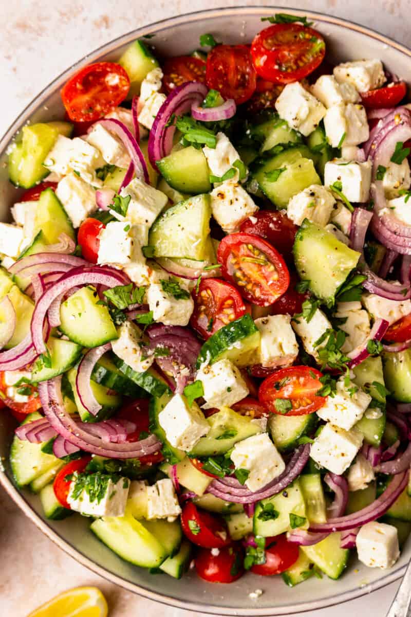 sliced cucumbers, tomatoes, feta, and red onion piled up in a large bowl