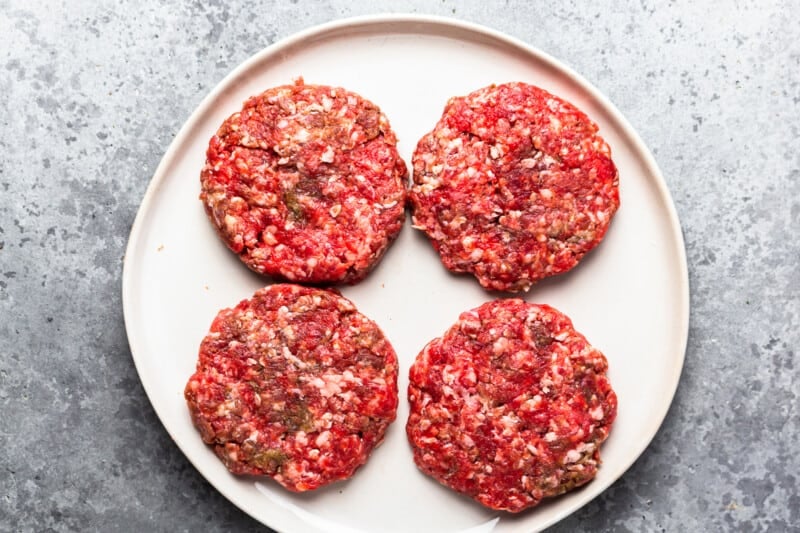 four uncooked burger patties on a plate