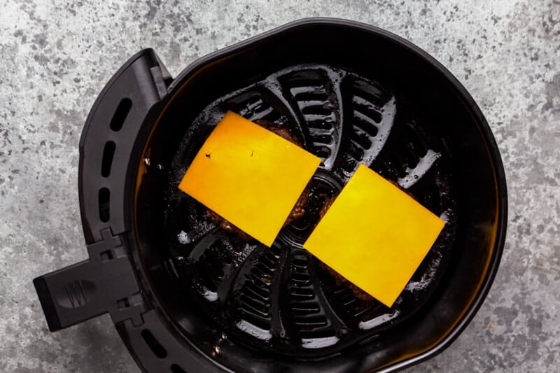 burger patties topped with cheese in the basket of an air fryer