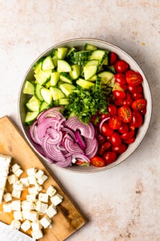 sliced up cucumbers, tomatoes, and red onions in a large bowl