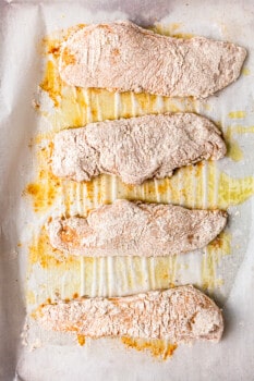 four pieces of chicken breast covered in flour and breading mixture