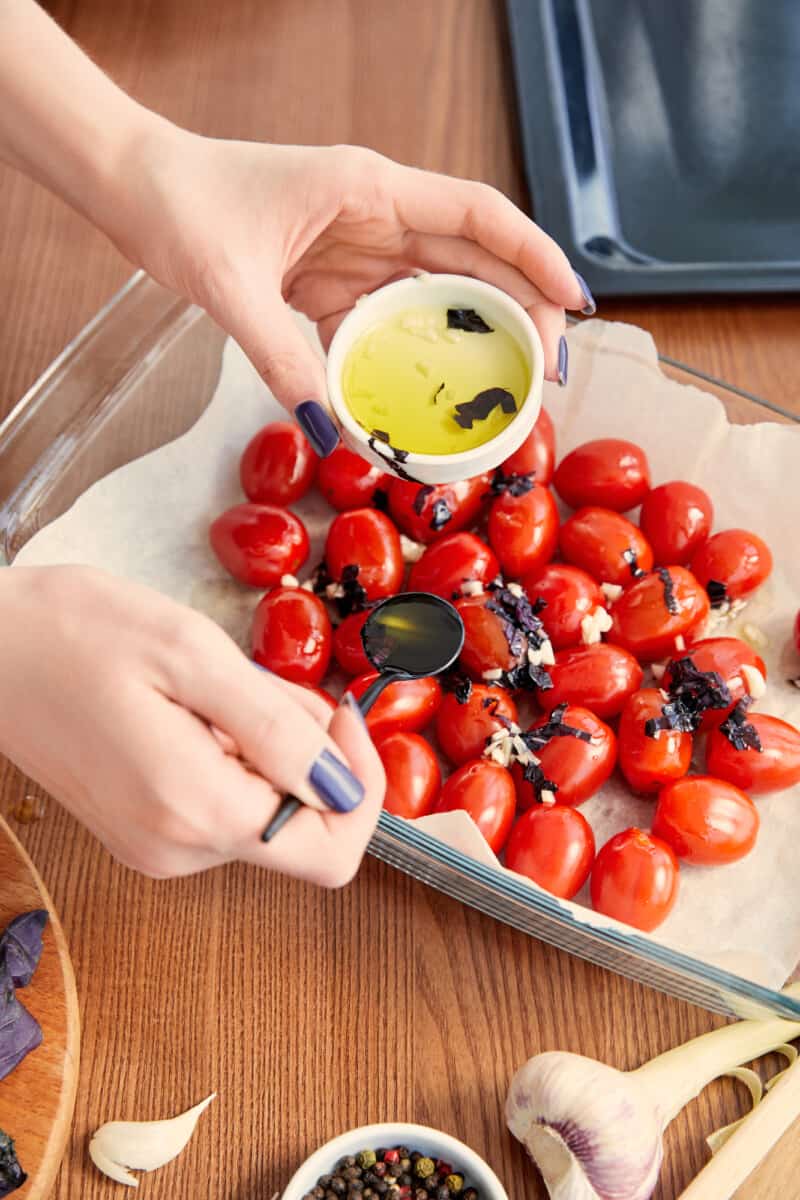 A woman pouring olive oil on tomatoes in a baking dish.