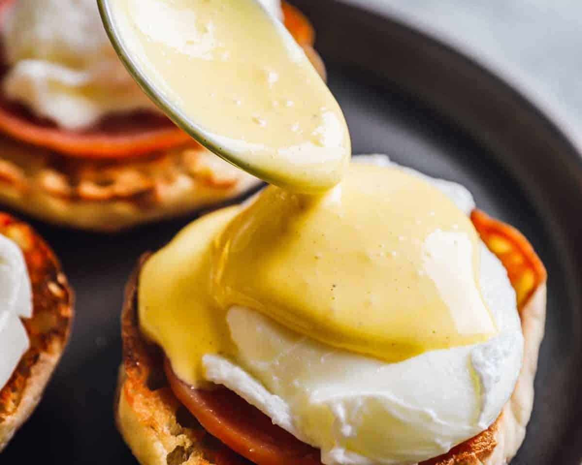 Pouring hollandaise sauce over the egg on the English muffin.