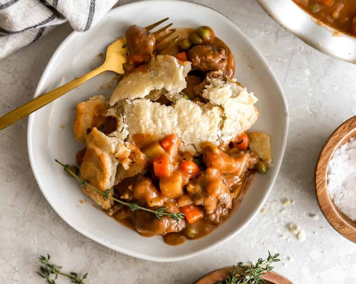 A slice of beef pot pie on a white plate with a gold spoon. - 11
