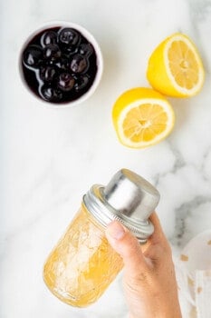 a hand shaking a whiskey sour in a mason jar shaker.