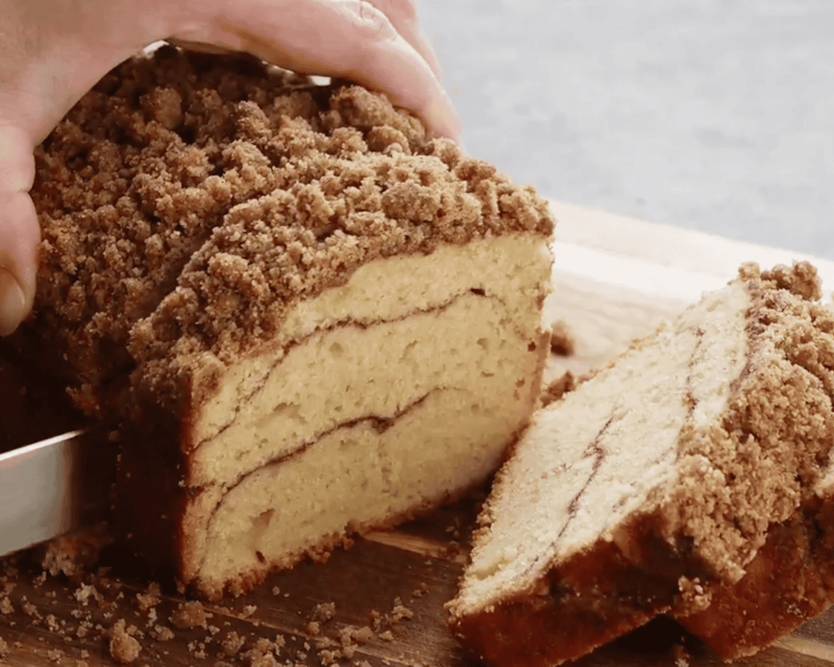 Hand holding cinnamon roll bread while slicing with a knife on a wooden cutting board
