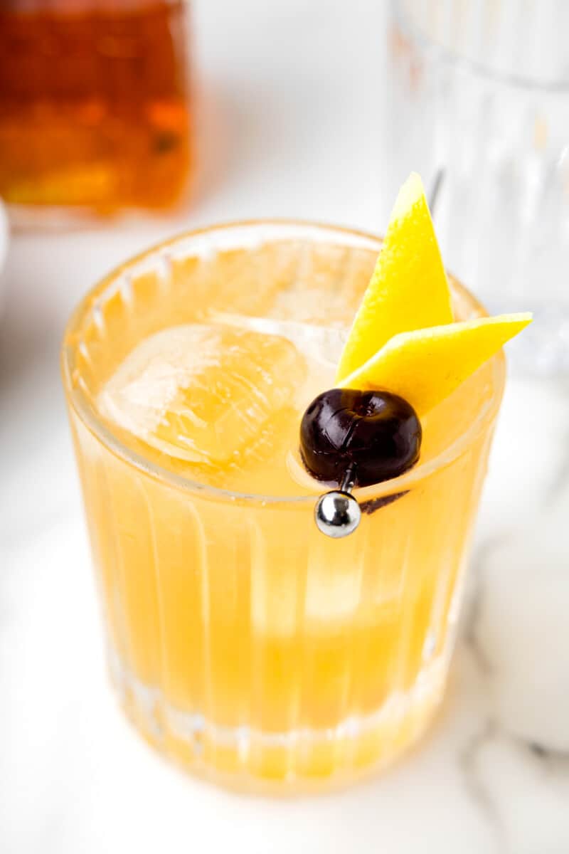 close up of whiskey sour with a cherry and lemon peel.