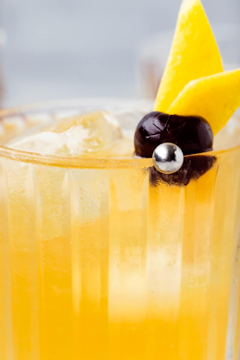 close up of a whiskey sour with a cherry and lemon peel.