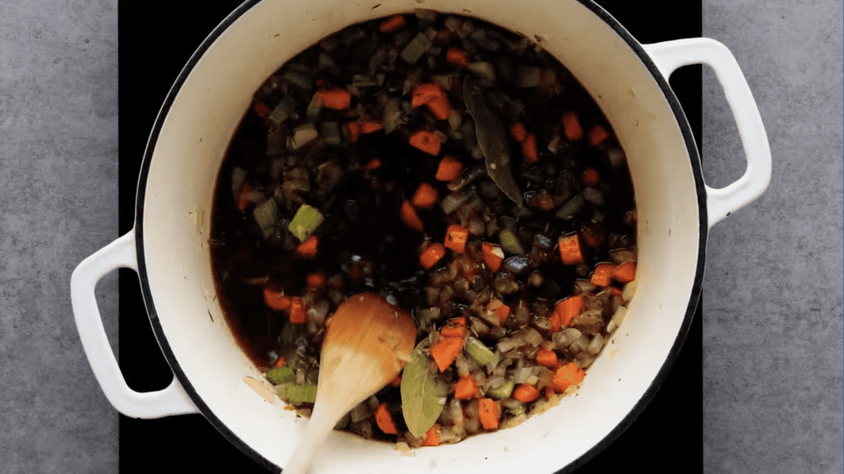 vegetables deglazed with red wine in a dutch oven with a wooden spoon.