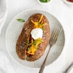 overhead view of a loaded air fryer baked potato on a white plate with a fork.