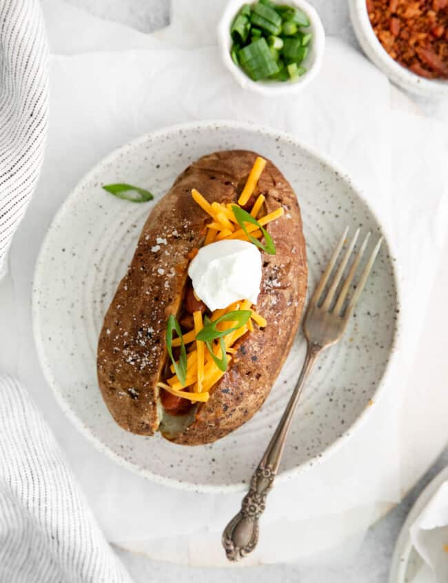 overhead view of a loaded air fryer baked potato on a white plate with a fork.