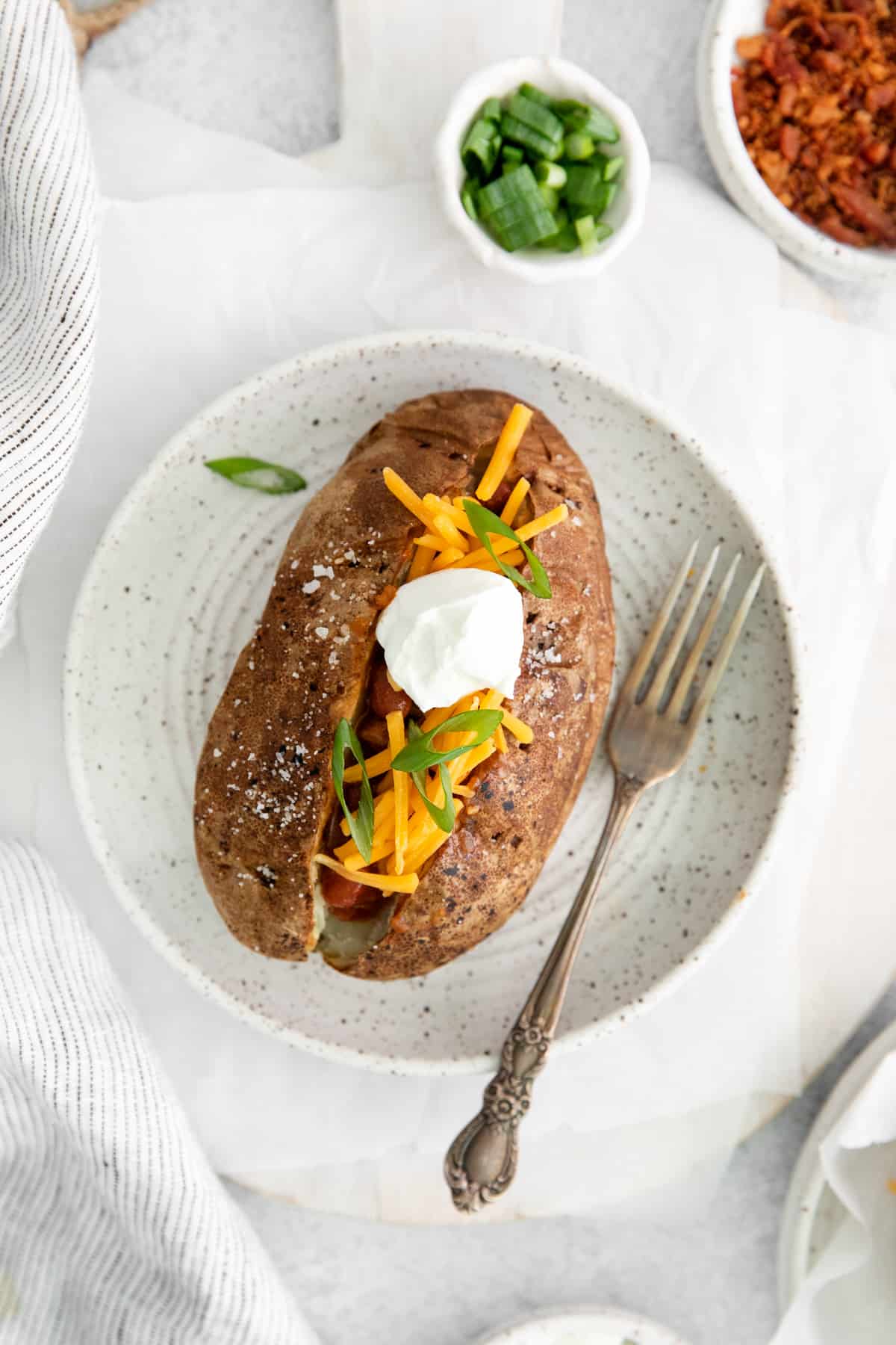 overhead view of a loaded air fryer baked potato on a white plate with a fork.