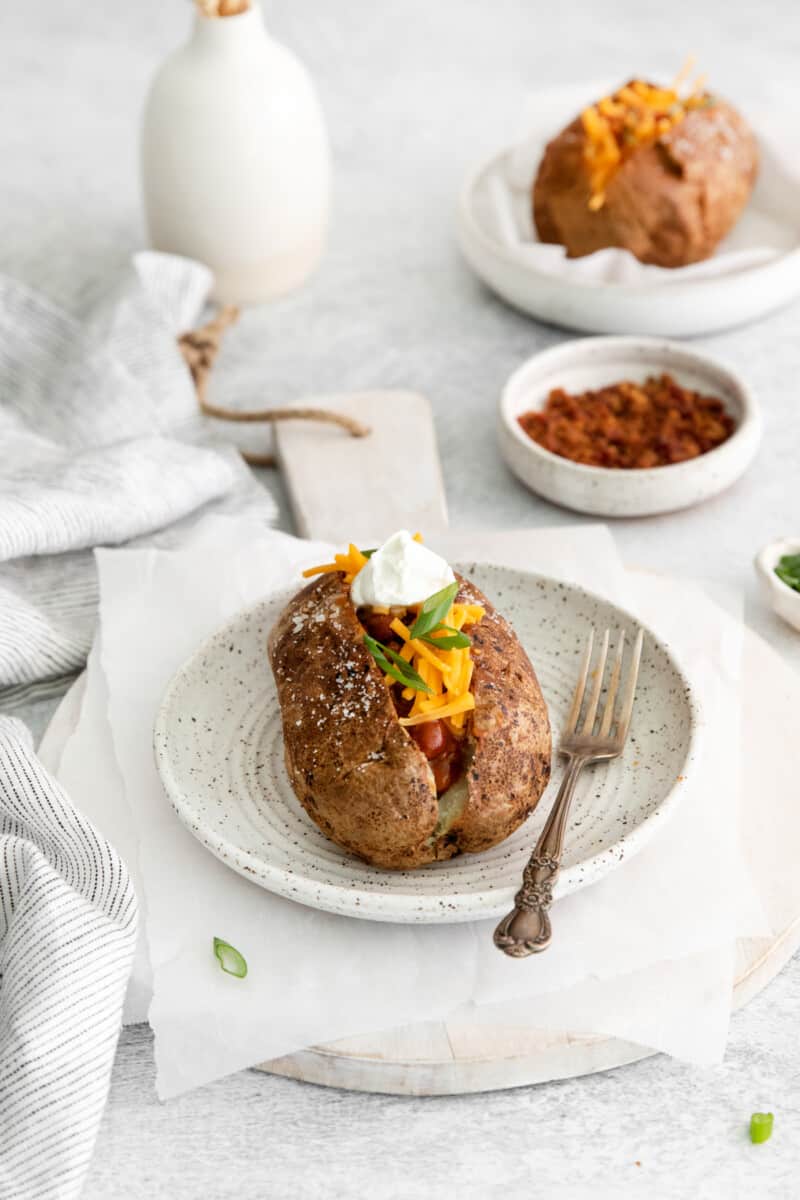 side view of a loaded air fryer baked potato on a white plate with a fork.