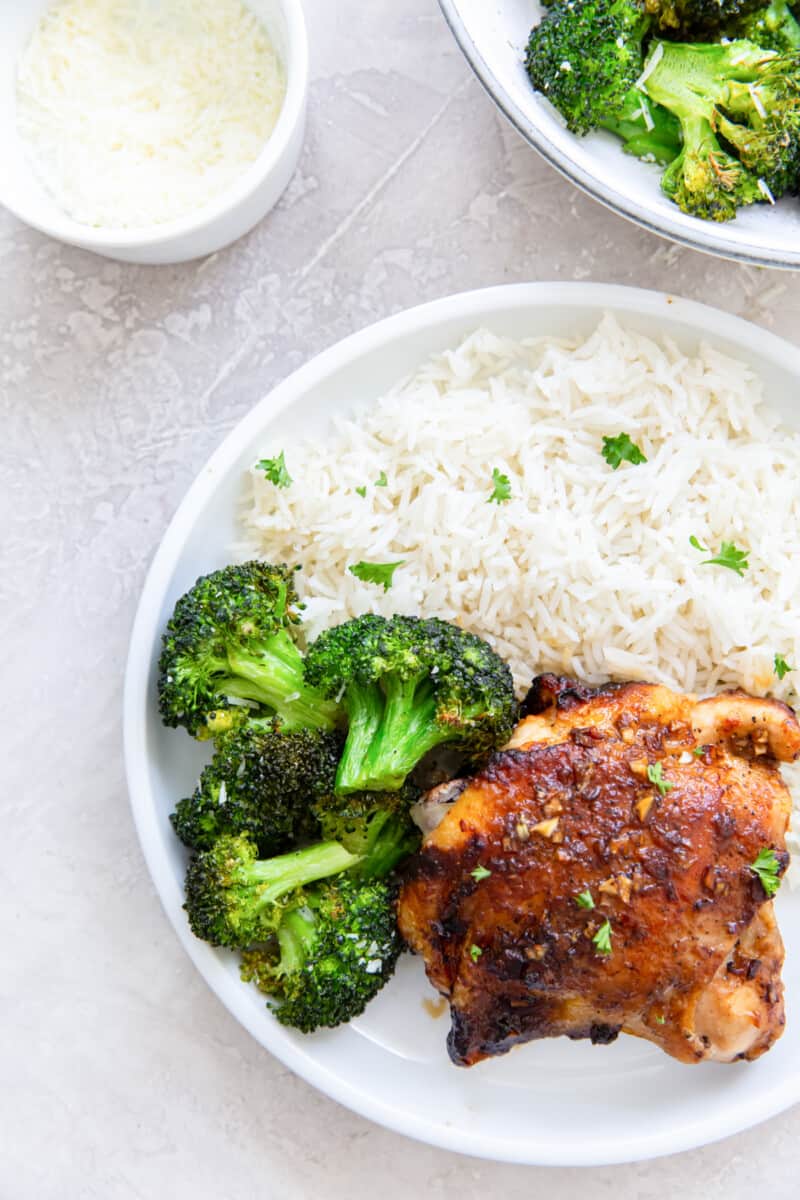overhead view of air fryer broccoli on a white plate with chicken and rice.