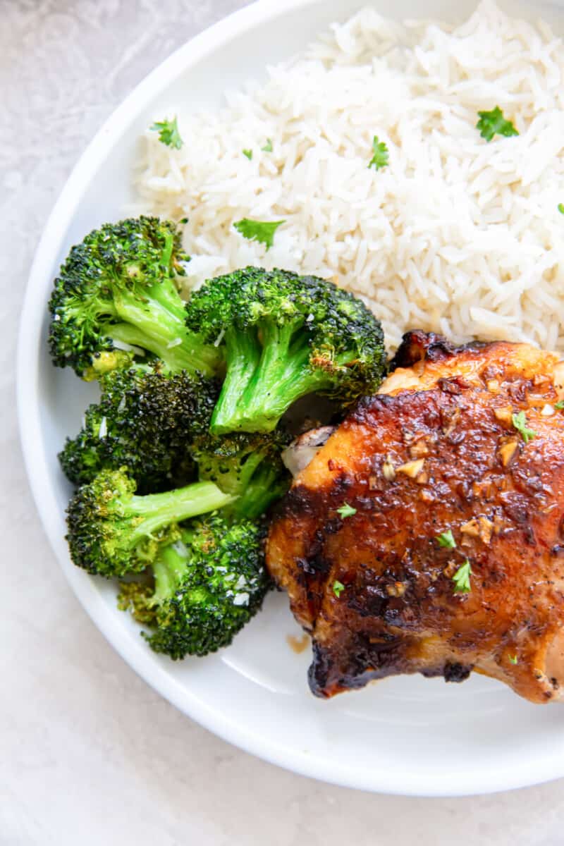 overhead view of air fryer broccoli on a white plate with chicken and rice.