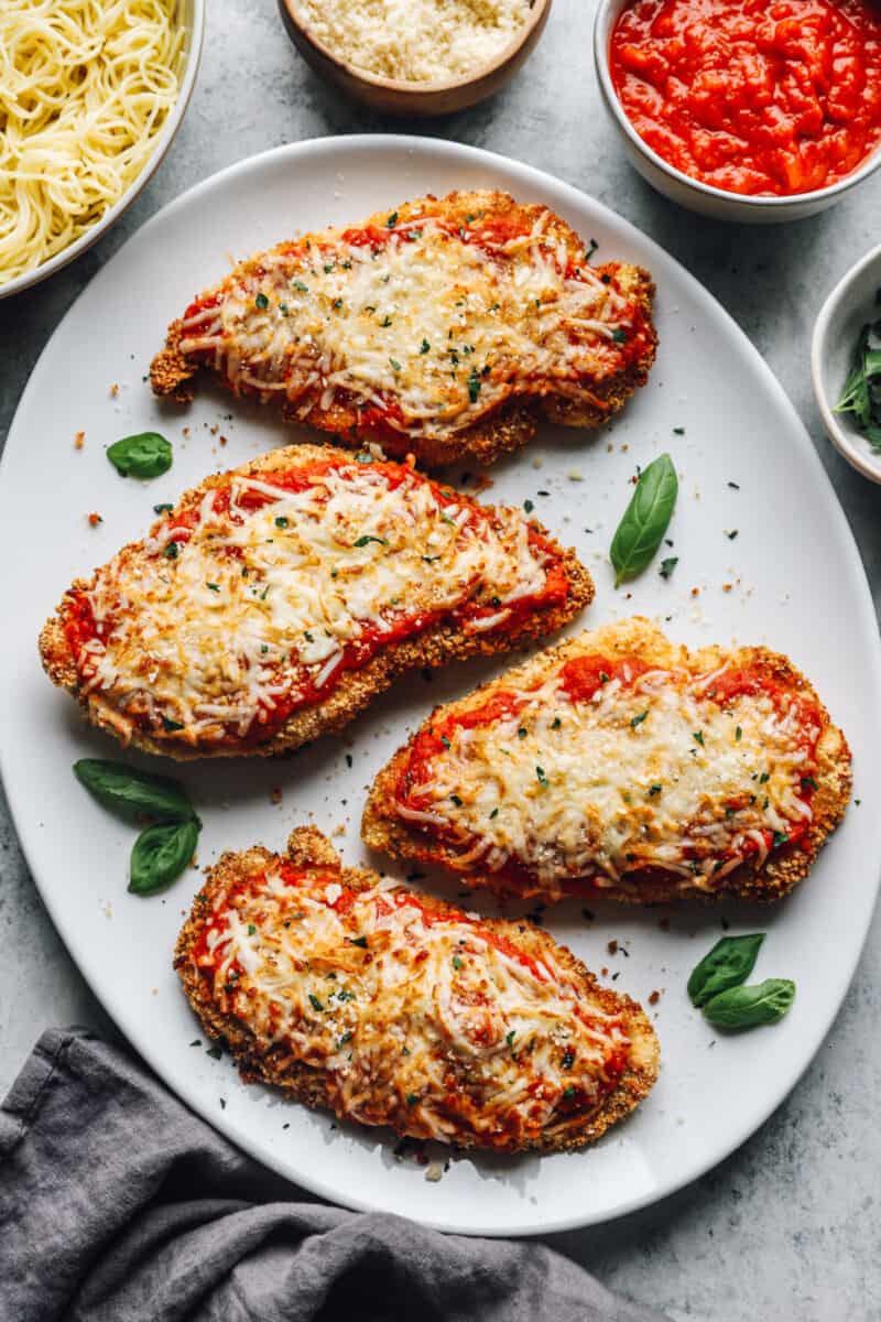 overhead view of 4 pieces of air fryer chicken parmesan on a white serving platter.
