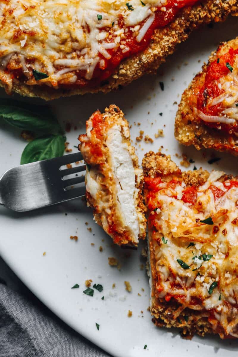 a forkful of air fryer chicken parmesan resting on a platter of air fryer chicken parmesan.