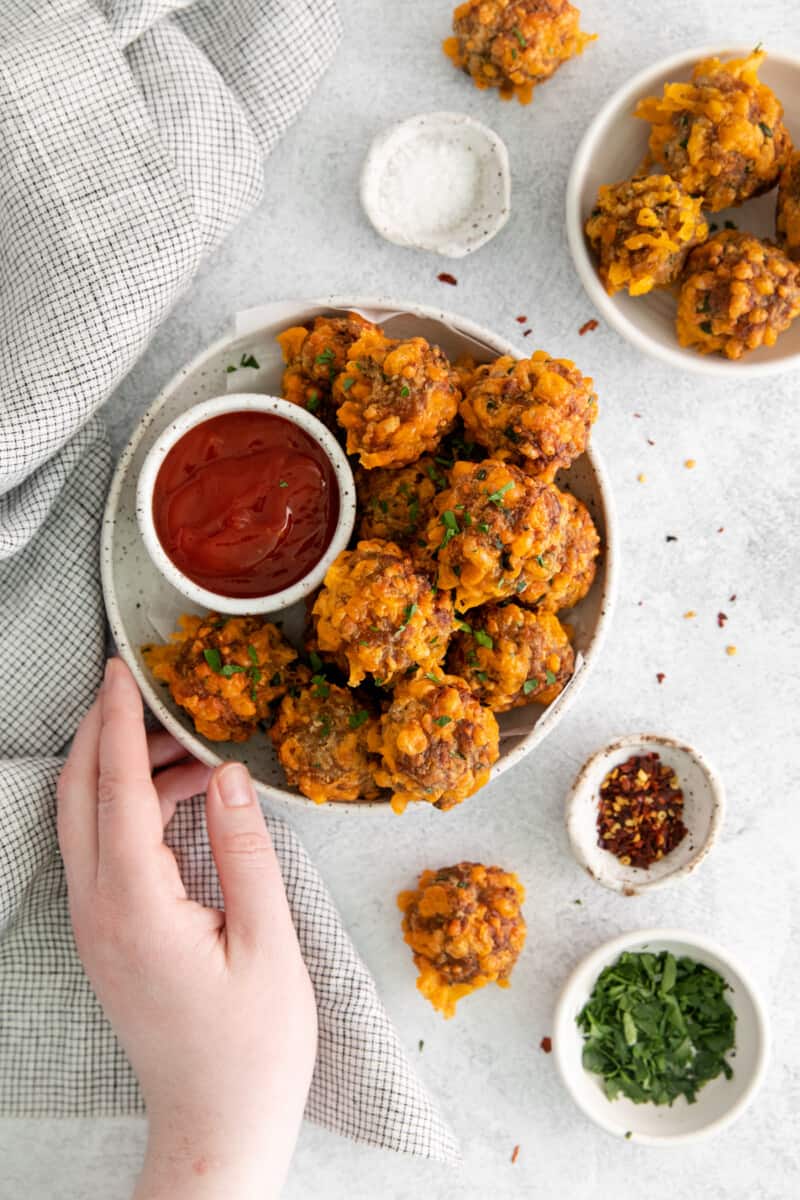 a hand holding a plate of air fryer sausage balls with sweet chili ketchup.