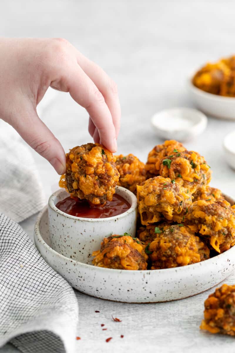 a hand dipping an air fryer sausage ball into sweet chili ketchup.