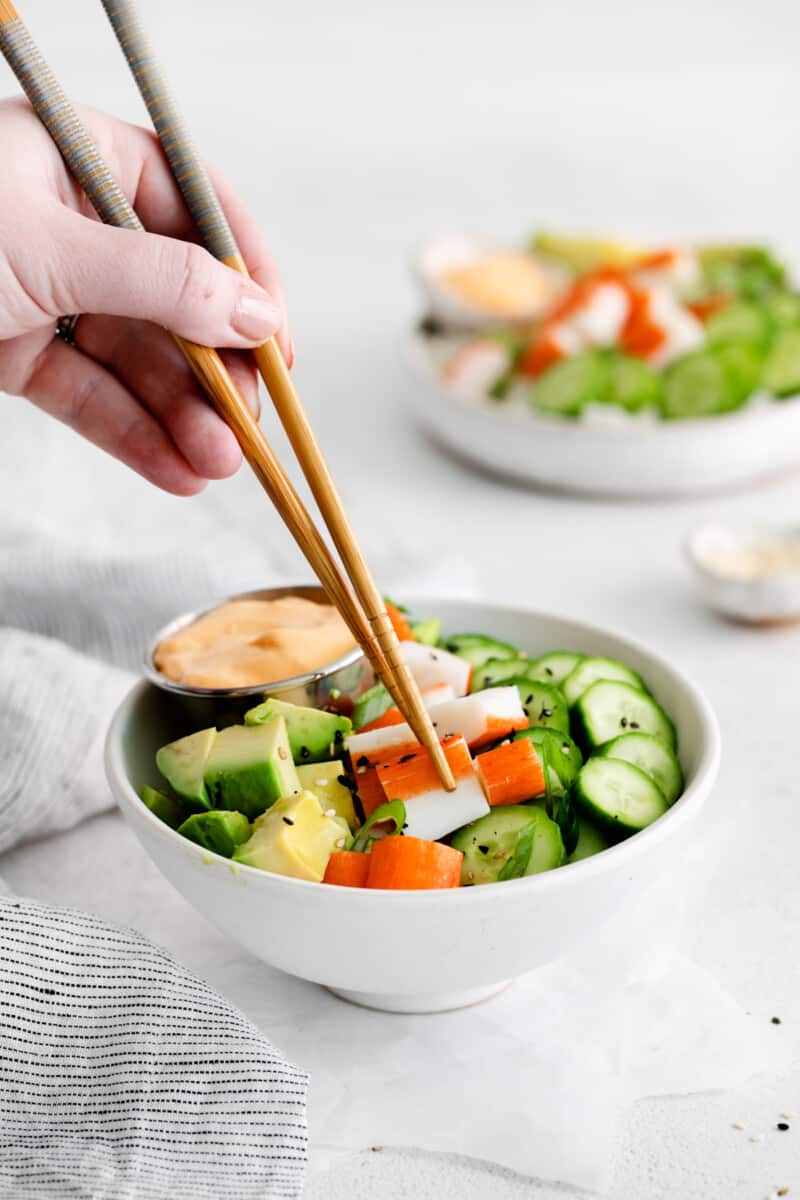 hand holding chopsticks, and picking up a piece of imitation crab out of a sushi bowl