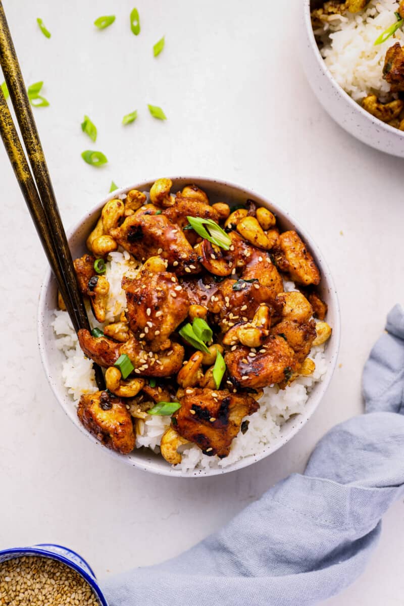 cashew chicken in a white bowl with chopsticks.