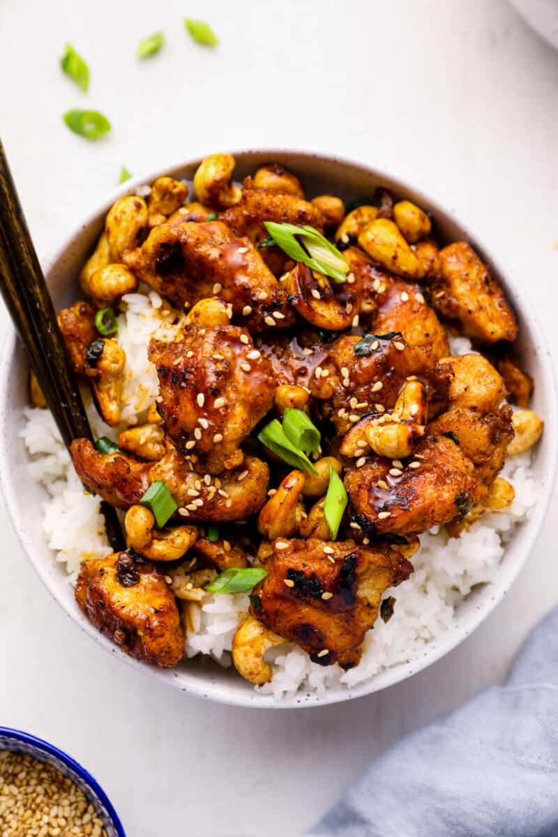 close up of cashew chicken in a white bowl with chopsticks.