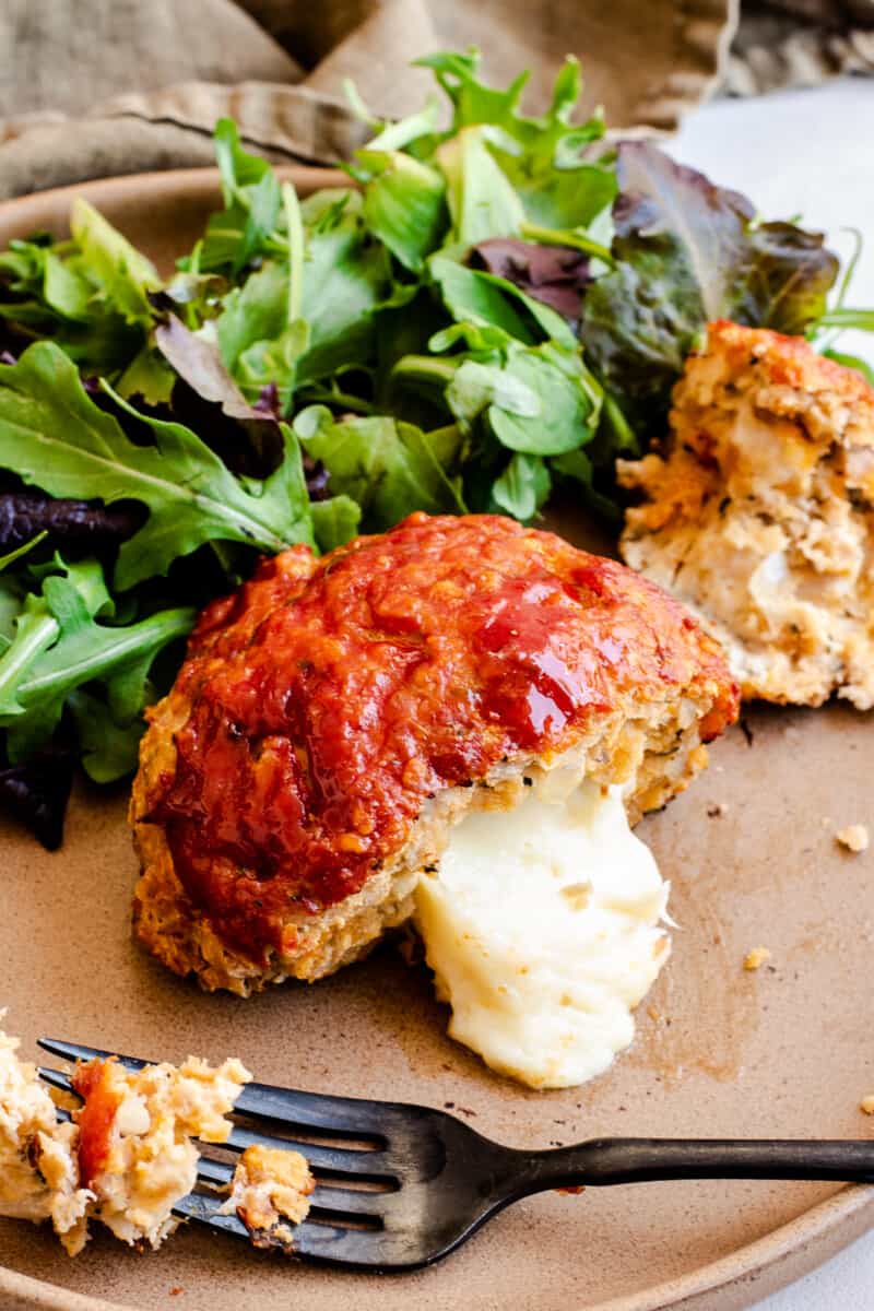a cheese-stuffed individual-sized meatloaf cut in half, on a plate of greens
