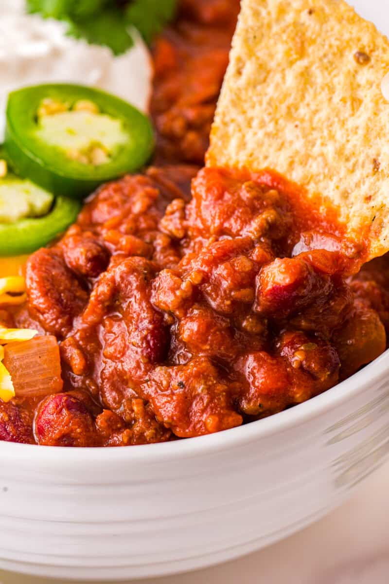 a tortilla chip scooping chili con carne out of a white bowl.