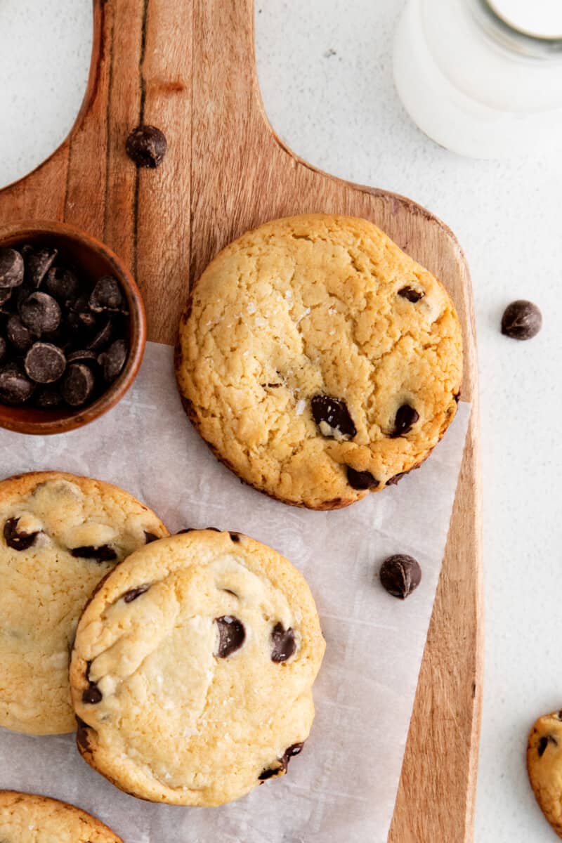 close up of cake mix chocolate chip cookies on a cutting board with a cup of chocolate chips.