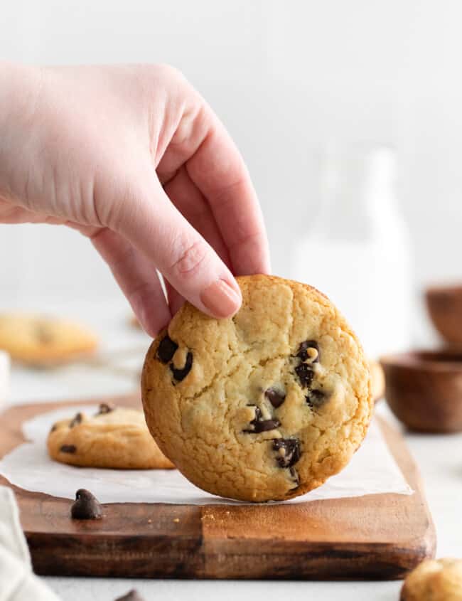 a hand holding a cake mix chocolate chip cookie vertically on a cutting board.