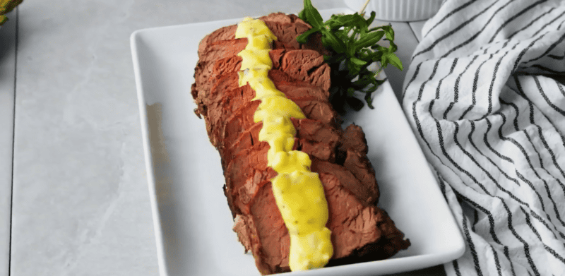 Beef tenderloin with Bearnaise sauce on a platter garnished with tarragon leaves.