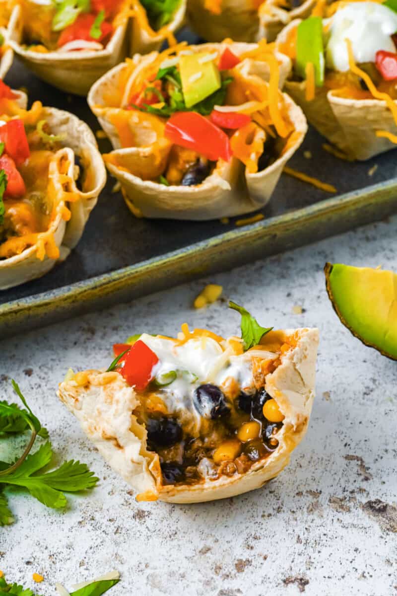 1 enchilada cup on a countertop in front of a tray of enchilada cups.