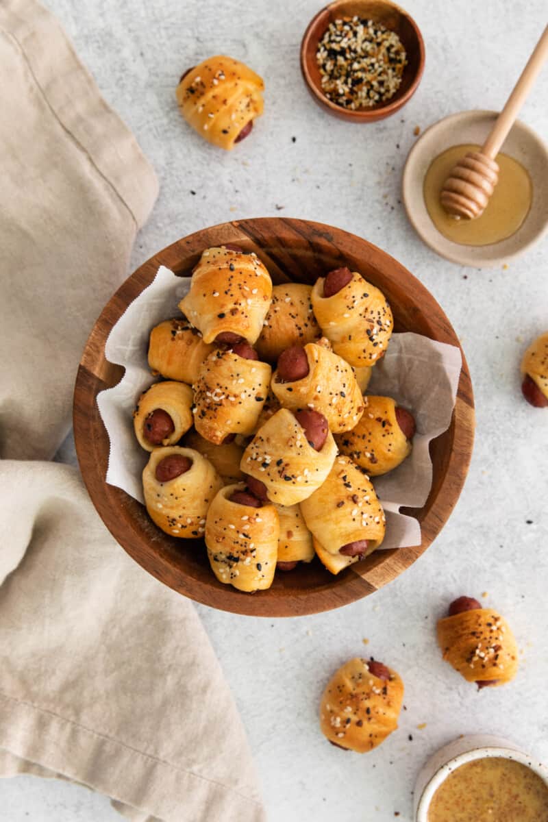 a bowl of pigs in a blanket in the center of a table, surrounded by bowls of ingredients and a cloth napkin