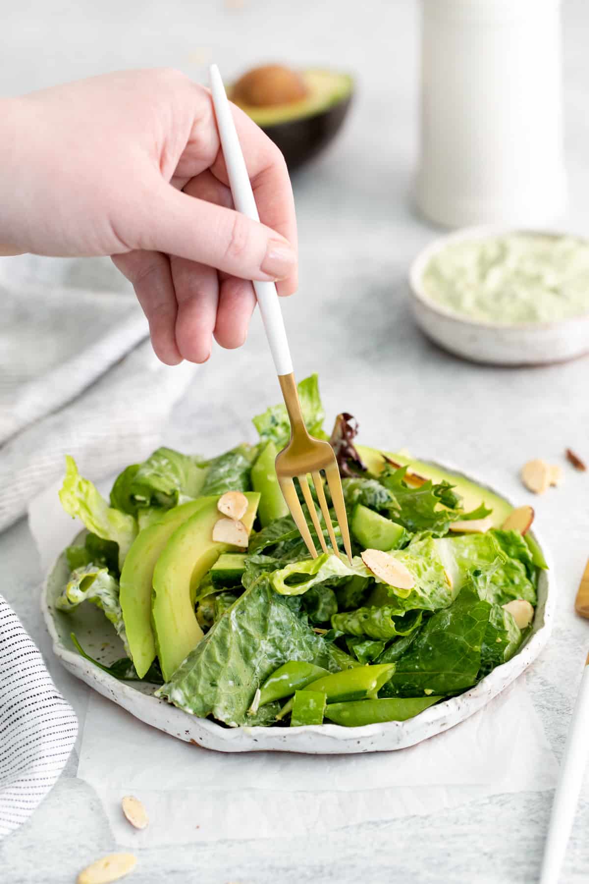 hand holding a fork, picking a piece of lettuce from a plate of salad