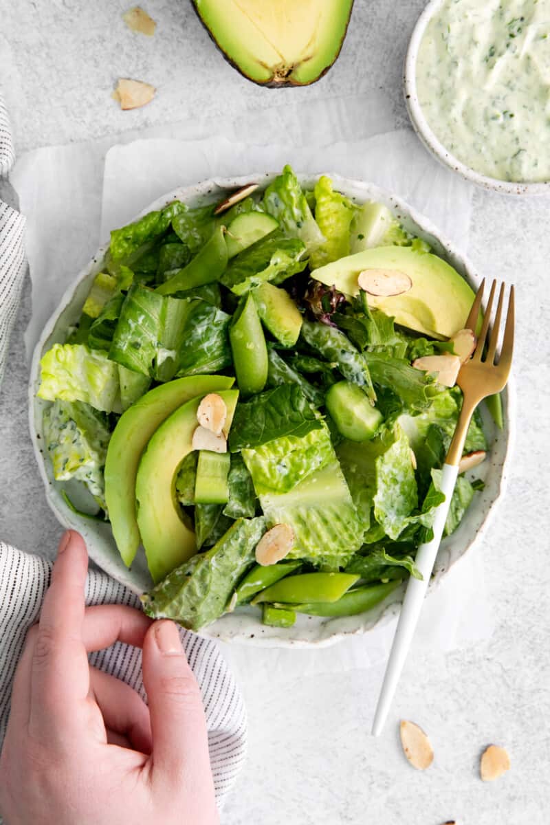 a hand reaching towards a bowl of green salad