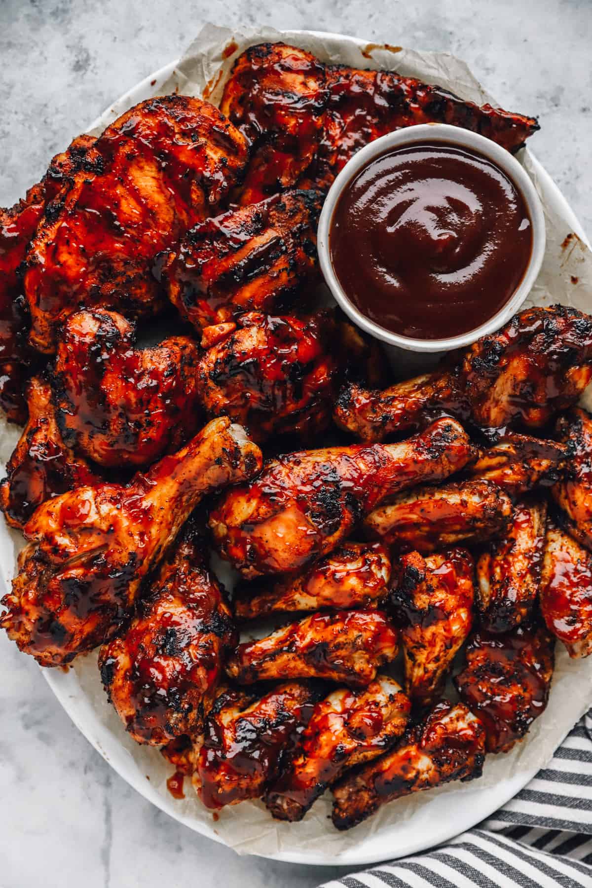 a plate of grilled BBQ chicken pieces, with a small bowl of BBQ sauce