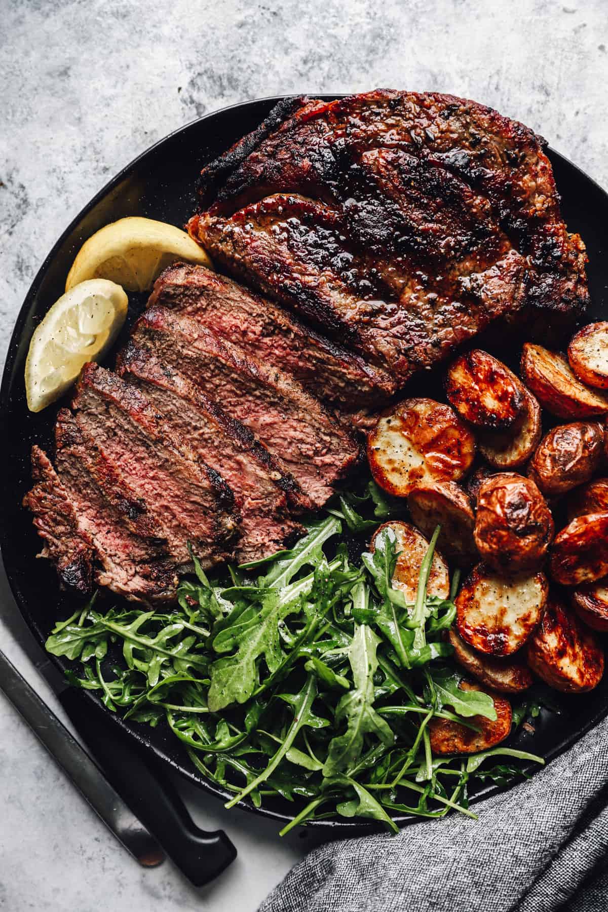 a plate with grilled ribeyes, greens, and potatoes