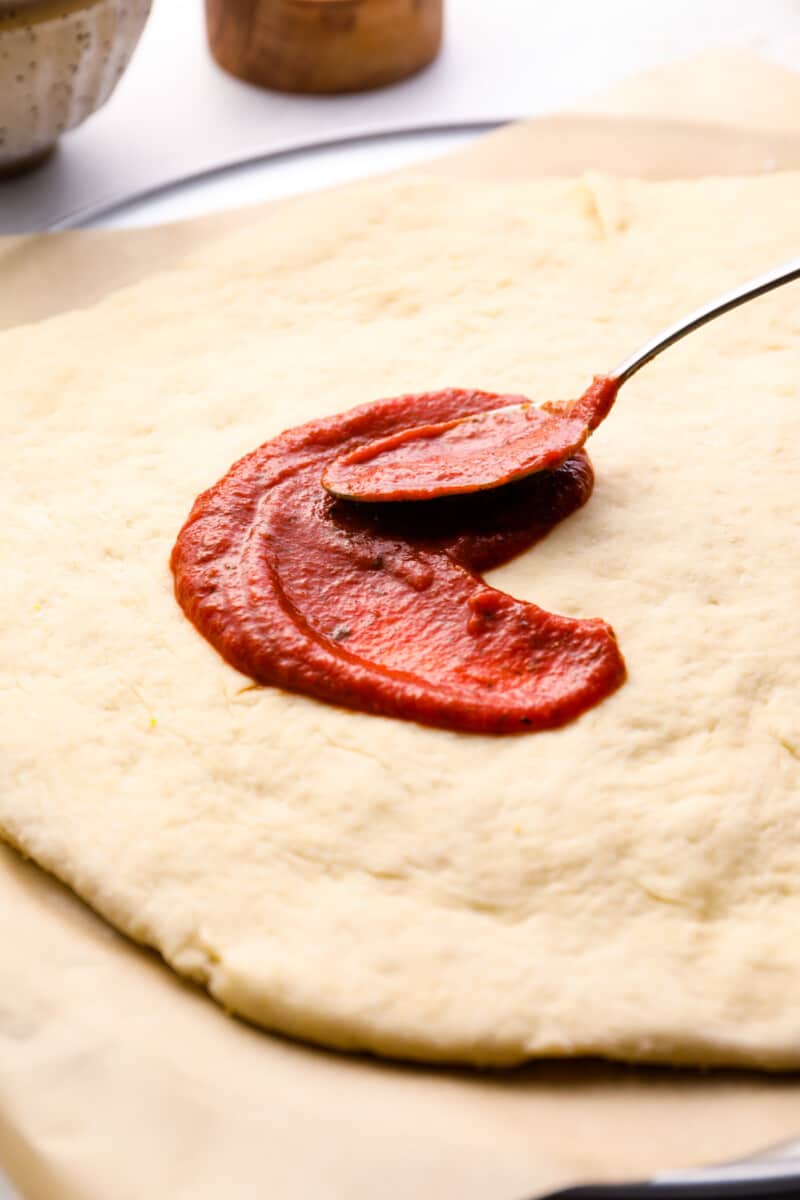 spreading tomato sauce on homemade pizza dough