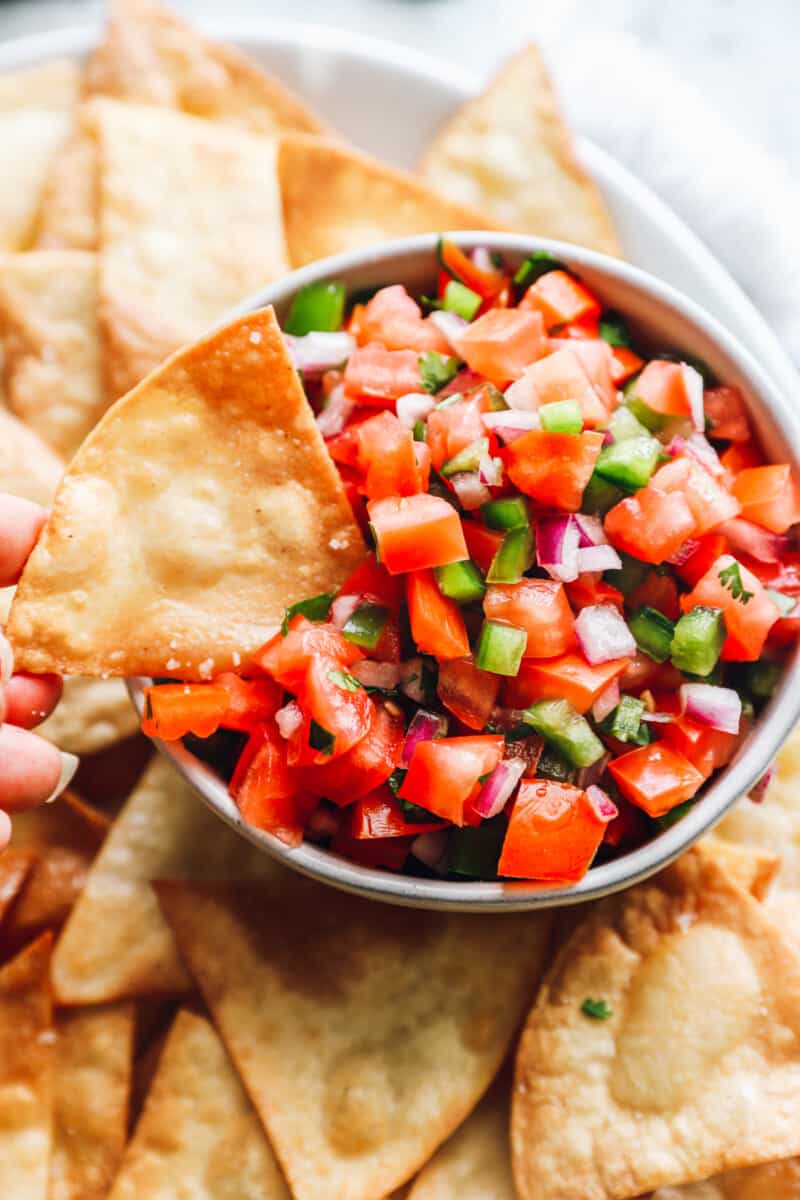 a homemade tortilla chip being dipped into a bowl of salsa.