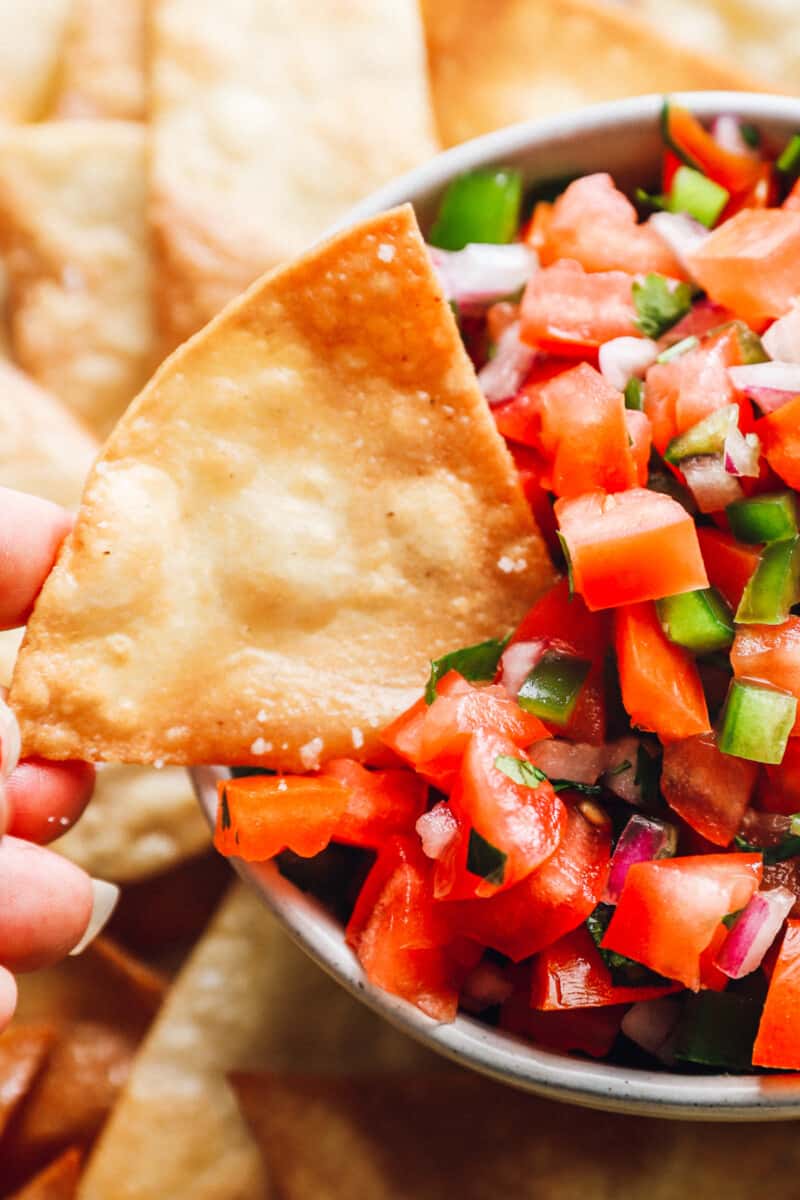 a homemade corn tortilla chip being dipped into a bowl of salsa.