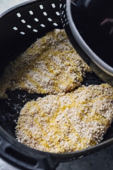 2 breaded chicken breasts in the basket of an air fryer.