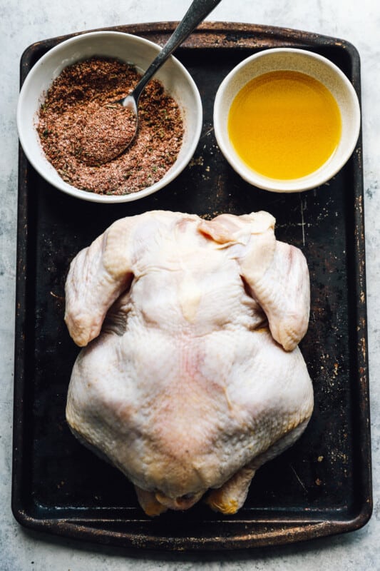 uncooked chicken on a pan, next to two bowls filled with ingredients to season it