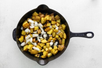 onion added to cooked diced potatoes in a cast iron skillet.