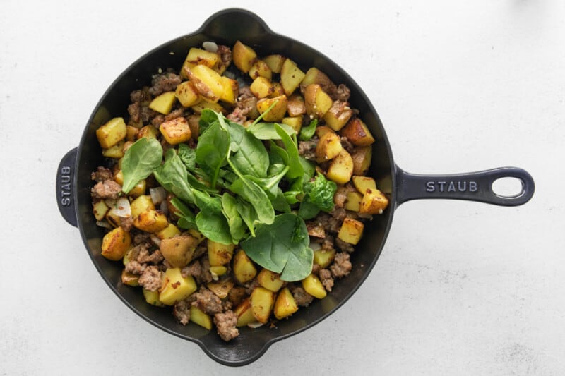 spinach added to breakfast hash in a cast iron skillet.