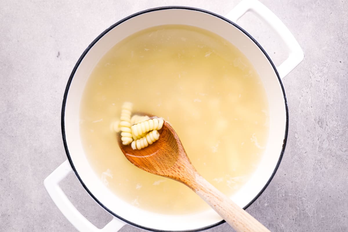 pasta boiling in starchy water with a wooden spoon.