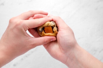 hands molding cookie dough around a square of caramel
