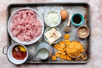 ingredients for cheesy turkey meatloaf arranged in small bowls, set on a baking tray