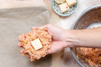 hand holding out a ball of meatloaf mixture, with a. square of melting cheese in the middle