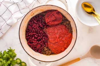 beans, crushed tomatoes, and tomato paste added to chili con carne in a dutch oven.