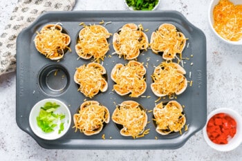 cheese added to enchilada cups in a muffin tin.